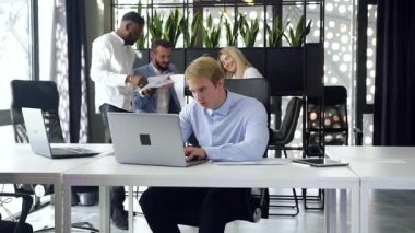 Modern ofisin iş yerindeki bilgisayarını kullanarak iş arkadaşlarının arka planında yavaş hareket eden zeki bir ofis çalışanı.