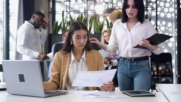 Sluiten van twee aantrekkelijke, zelfverzekerde zakenvrouwen die samenwerken in het kader van een gezamenlijk project in de kantoorruimte — Stockvideo