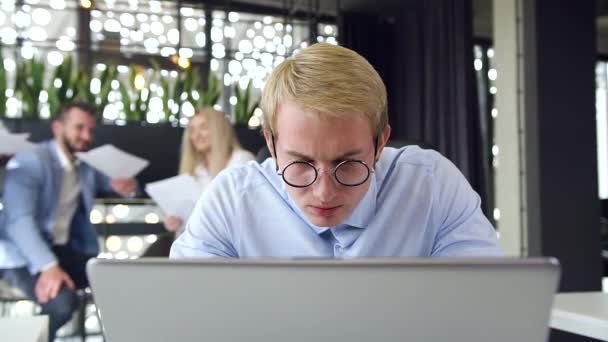 Крупный план занятого молодого бизнесмена в очках, работающего за компьютером в офисе — стоковое видео
