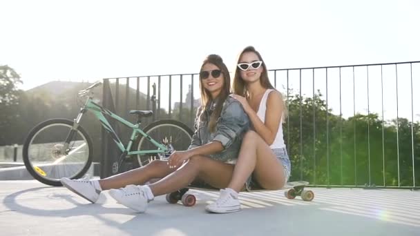 Κομψό και όμορφα κορίτσια φορώντας σαγηνευτική ενδυμασία που είναι οι καλύτεροι φίλοι, κάθεται σε skateboards και posung στην κάμερα — Αρχείο Βίντεο