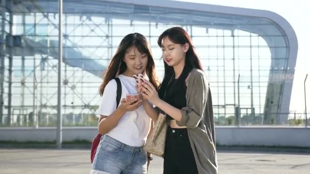 Charme jeunes filles asiatiques en vêtements décontractés avec des téléphones debout près de l'aéroport — Video