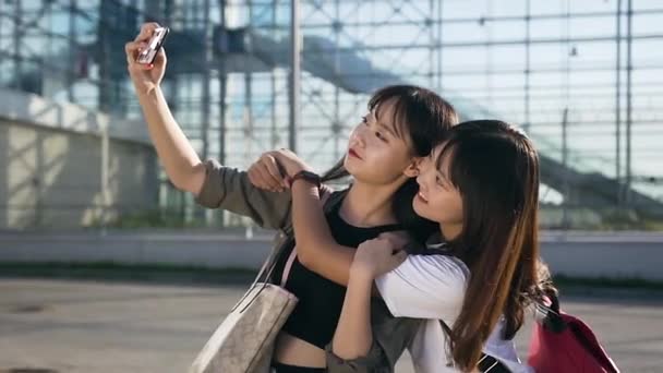 Aantrekkelijk portret van twee beste vrienden aziatische meisjes maken selfie met oprecht glimlachen op de luchthaven gebouw achtergrond — Stockvideo