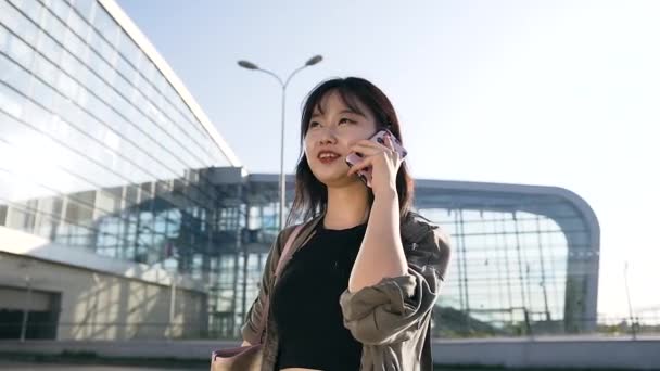 魅力的な若いアジアのブルネットの美しい肖像画空港ビルの近くの電話で話している長い髪 — ストック動画