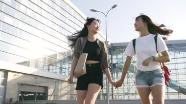 Modern havaalanının yakınında el ele tutuşup koşan, şık giyimli, neşeli, güzel Asyalı genç kızların ön görüntüsü.