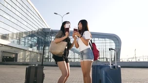 Привлекательные улыбающиеся 25-летние азиатские девушки радуются, находясь рядом со зданием аэропорта — стоковое видео
