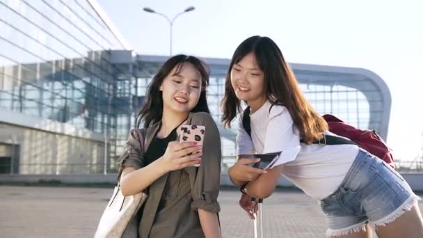 Encantador alegre 25s asiático feminino viajantes de pé perto moderno aeroporto e usando seus smartphones — Vídeo de Stock