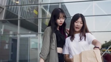 Gülümseyen güzel Asyalı bir kız, alışveriş merkezinden aldığı neşeli bayan arkadaşına komik oyuncağını gösteriyor.