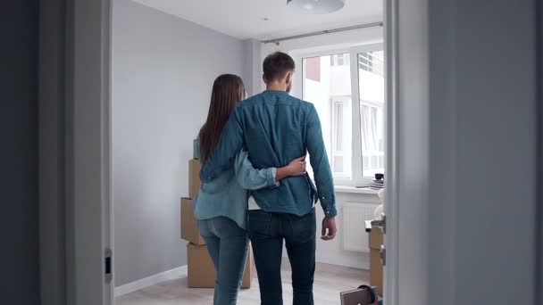 Pohled zezadu na atraktivní zamilovaný pár, který se objímá a přibližuje k velkému oknu ve svém novém bytě — Stock video