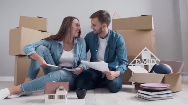 Slow motion of appealing amorous young couple which sitting on the floor and planning about their new life in new apartment — Stockvideo