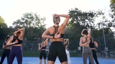 Şehir binalarının yakınındaki fitness eğitimi sırasında kollarını arkadan sıkan tanınmayan genç spor kadınların arka planı.