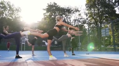 Şehir parkındaki spor sahasında denge egzersizleri yapan yedi güzel kadının yan görüntüsü.