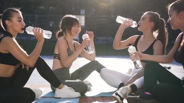 Καλαίσθητα αθλητικά λεπτά κορίτσια σε αθλητικά είδη κάθονται στο πάτωμα του σταδίου και πόσιμο νερό μετά την προπόνηση φυσικής κατάστασης — Αρχείο Βίντεο