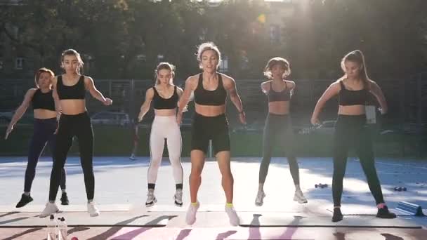 Frontansicht einer weiblichen Fitnessklasse, die beim Sport-Workout auf dem Freiluftstadion Sprungübungen macht — Stockvideo