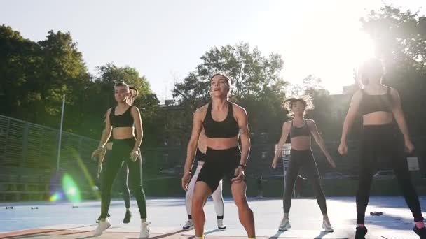 Fitness tým dobře vypadající štíhlé sportovní ženy dělá skákání dřepy na jejich sportovní cvičení na venkovním stadionu — Stock video