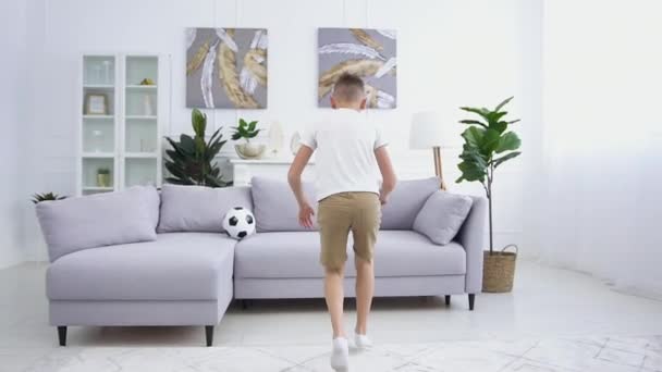 Active good-looking smiling 12-aged boy running up to the sofa in the living -room and making a rack on it — Stock Video