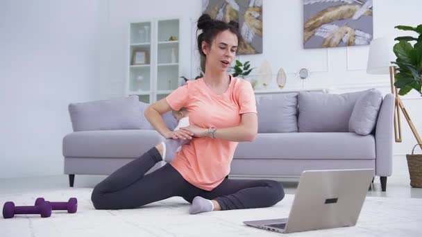 Agradable feliz pacífica mujer de 25 años mostrando ejercicios de fitness sentado en el estiramiento en la alfombra en casa para su equipo de entrenamiento a través de videollamada en el ordenador portátil — Vídeos de Stock