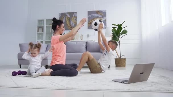 Likable tevreden zorgeloze jonge moeder helpen om oefeningen te doen met bal samen met haar actieve zoon en haar schattige kleine dochter interfereren haar — Stockvideo