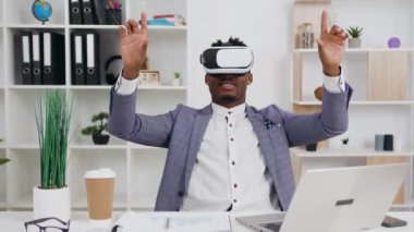 Yakışıklı, koyu tenli, şık elbiseli, iş yerinde oturan ve sanal gerçeklik kulaklığı takan adam, 4K