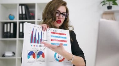 Güzel görünümlü 30 yaşında, kendine güveni tam bir iş kadını. Ofis odasındaki video görüntüleriyle iş ortağına finansal tabloları açıklıyor.