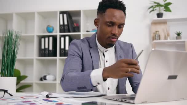 Hombre de negocios de piel negra con buena apariencia y confianza, sentado frente a la computadora y trabajando con información en pantalla, cámara lenta — Vídeos de Stock