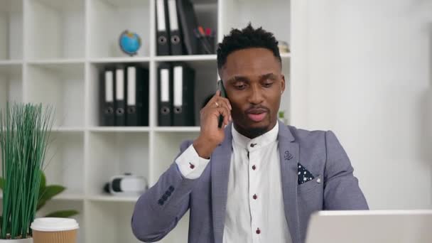 Close up of attractive smart confident young black-skinned office manager which has phone conversation in his contemporary office — Stock Video