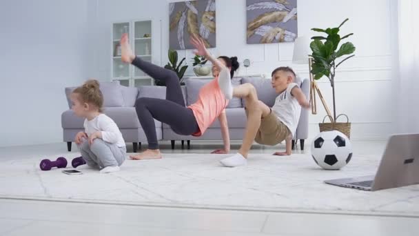 Alegre satisfeita ativa esportiva mãe e filho fazendo exercícios esportivos, enquanto pequena menina adorável jogando perto deles — Vídeo de Stock