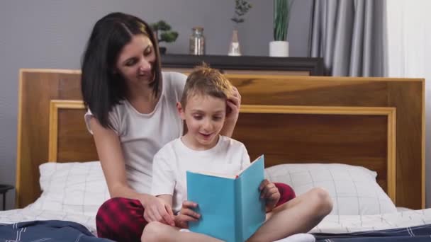 Belle maman souriante heureuse et fils passent leur temps libre ensemble à lire un livre intéressant à la maison — Video