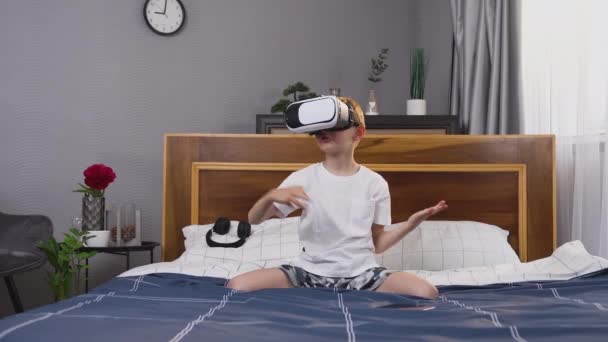 Vista frontal de niño amigable de buena naturaleza en camiseta y pantalones cortos que juegan juego con auriculares de realidad virtual en casa — Vídeo de stock