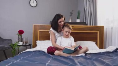 Çekici gülümseyen, uyurgezer anne, 8 yaşındaki yakışıklı oğluyla birlikte yatakta kitap okuyor.