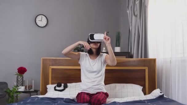 漂亮而严肃的穿着睡衣的年轻黑发姑娘坐在卧室的床上，用特殊的3D眼镜在虚拟屏幕上工作 — 图库视频影像