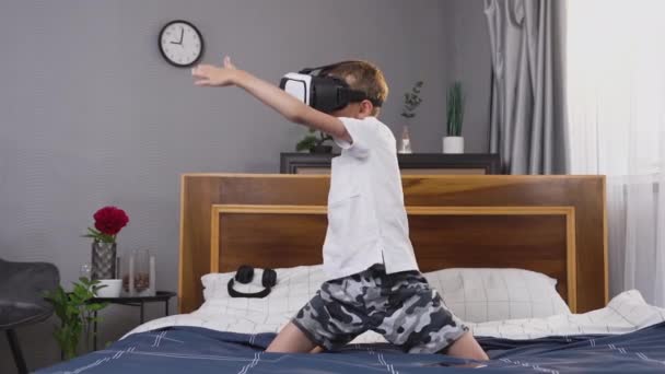 Guapo niño sonriente emocional en ropa de casa estar en el dormitorio y jugar a videojuegos con gafas 3D virtuales especiales — Vídeo de stock