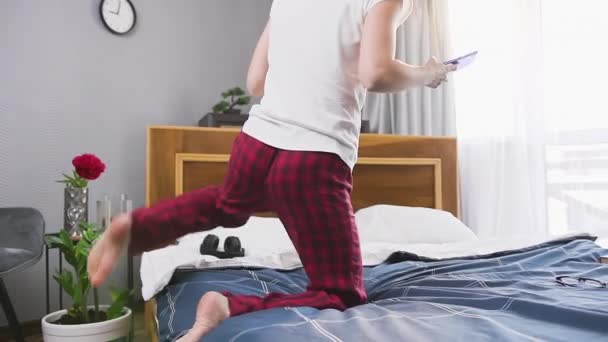 Attraktive dunkelhaarige positive junge Frau im Pyjama, die mit einer Tasse Tee auf dem Schlafzimmerbett sitzt und das Smartphone benutzt — Stockvideo