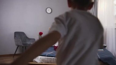 Yakışıklı, gülümseyen küçük çocuk mutlu annesine koşuyor ve onunla yatağa düşüp gülüyor.