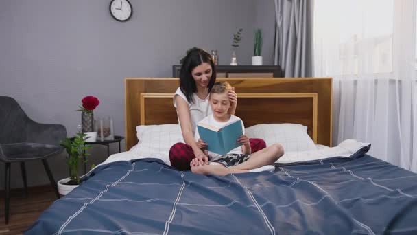 Close up of high-spirited lucky attractive mother and son which spending their free time with interesting book at home — Stock Video