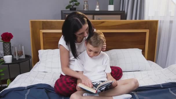 Portrait of contented likable happy smiling mom and son which reading together interesting book at home — Stock Video