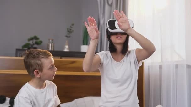 Крупным планом сконцентрирована уверенная в себе женщина 30 лет с темными волосами, которая работает на воображаемом экране, применяя специальные виртуальные 3D очки и красивый сын 8-летнего возраста наблюдая за ней — стоковое видео