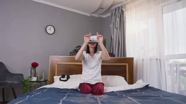 Primer plano de adorable enfocado mujer joven ocupada en ropa de casa que se sienta en la cama del dormitorio y trabajando en la pantalla imaginaria usando gafas especiales 3d — Vídeo de stock