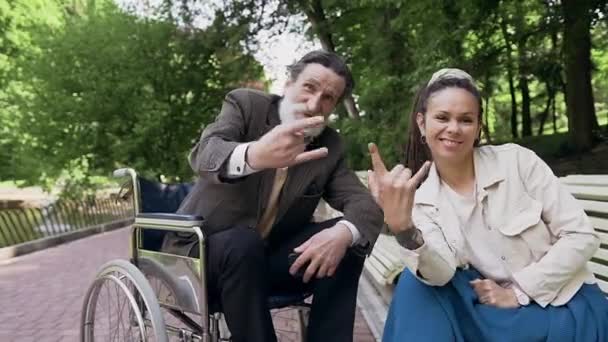 Front view of attractive happy smiling modern grandaughter with dreadlocks and her positive handsome bearded old granddad which posing on camera with youthful gestures in green park — Stock Video