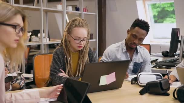 Вид спереду на сфокусовану приємну творчу молоду багаторасову команду чоловіків і жінок, яка працює разом у сучасній офісній кімнаті — стокове відео