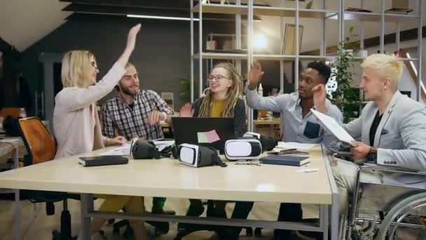 Çalışmaya başlamadan önce iş yerinde oturup beşlik çakan çok ırklı arkadaşlardan oluşan güzel görünüşlü, gülümseyen bir grubun ön görüntüsü. — Stok video