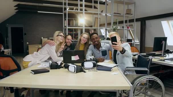 Красивый счастливый креативный современный офис молодых людей делает селфи по телефону, сидя за рабочим столом в современном офисе — стоковое видео