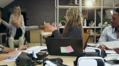 Çekici, memnun, çok ırklı iş arkadaşları tekerlekli sandalyedeki erkek arkadaşını selamlıyor ve ona çağdaş ofis odasında beşlik çakıyor.