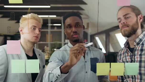 Jóképű tapasztalt kreatív változatos férfi csapat ötletelés különböző verziók üveg falon a kortárs irodai szobában — Stock videók