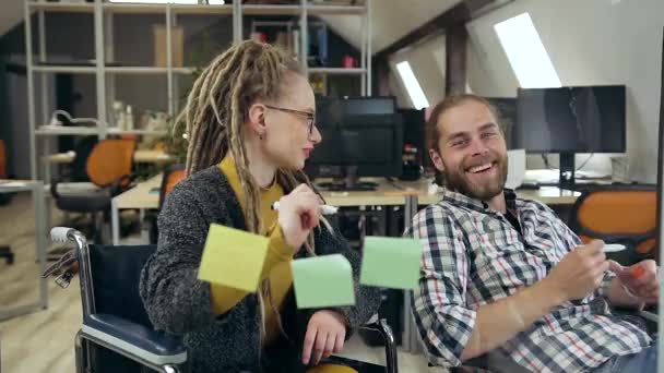 Vista próxima de amigável sorrindo atraente jovens colegas do sexo masculino e feminino que trabalham juntos sob projeto conjunto usando parede de vidro no escritório moderno — Vídeo de Stock