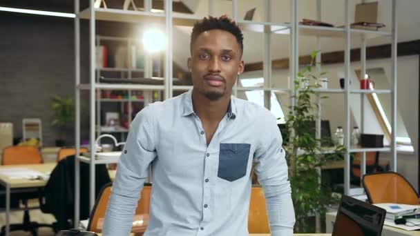 Front view of handsome confident black-skinned young man which standing on office room background with crossed hands and looking into camera with nice smile — Stock Video