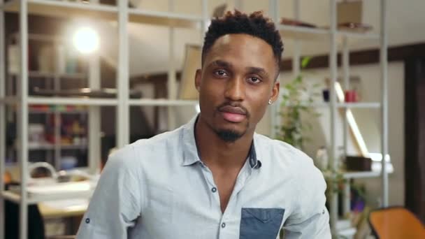 Good-tempered attractive concentrated young dark-skinned guy looking at camera with confident view in the contemporary office — Stock Video