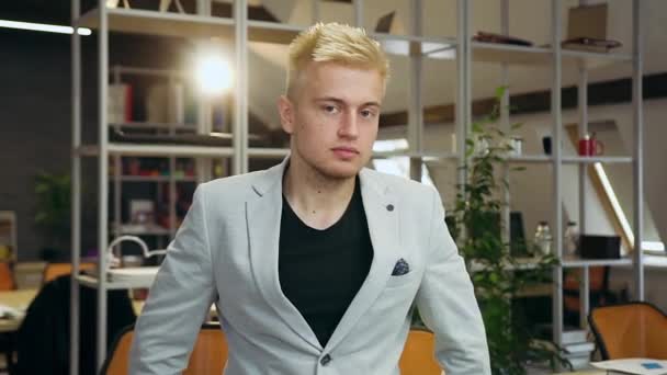 Handsome smiling light-haired stylish young man standing in contemporary office room and posing on camera with lucky smile — Stock Video