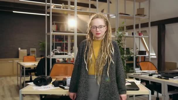 Atraente positivo confiante 30-aged trabalhador de escritório do sexo feminino com dreadlocks de pé perto de seu local de trabalho em sala de escritório moderno com braços cruzados e olhando para a câmera — Vídeo de Stock