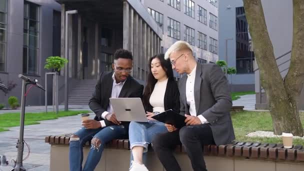 Visão frontal de boa aparência confiante sorrindo trabalhadores jovens colegas multiétnicos que trabalham com computador ao ar livre — Vídeo de Stock