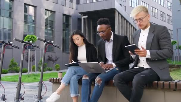 Gros plan de sympathique concentré moderne prudent mixte collègues de bureau qui travaillent sur le banc près de l'immeuble de bureaux dans le cadre d'un projet commun — Video